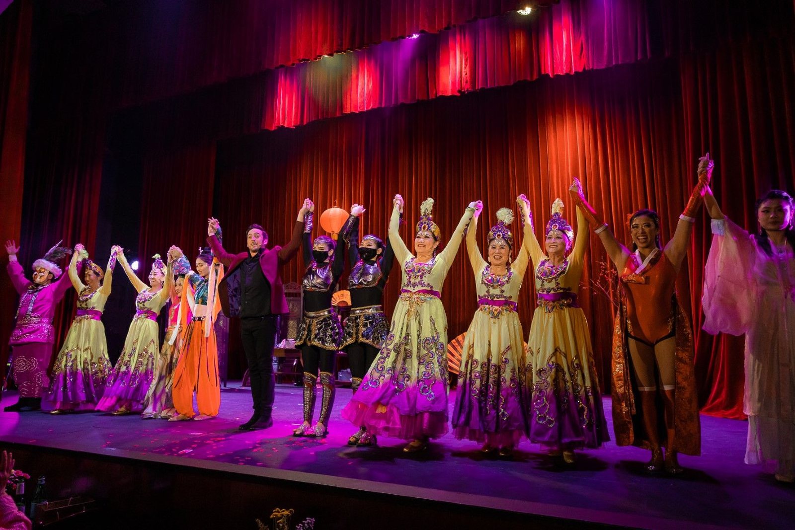 Performers in colorful, ornate costumes hold hands and raise their arms for a curtain call at the Great Star Theater.
